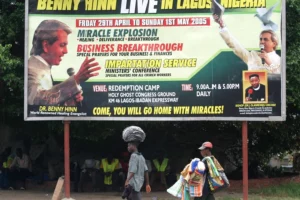 Street vendors walk past a billboard advertising visits by Pentecostal preachers to Nigeria on April 13, 2005 in Lagos, Nigeria. George Esiri/REUTERS