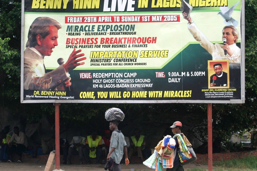 Street vendors walk past a billboard advertising visits by Pentecostal preachers to Nigeria on April 13, 2005 in Lagos, Nigeria. George Esiri/REUTERS